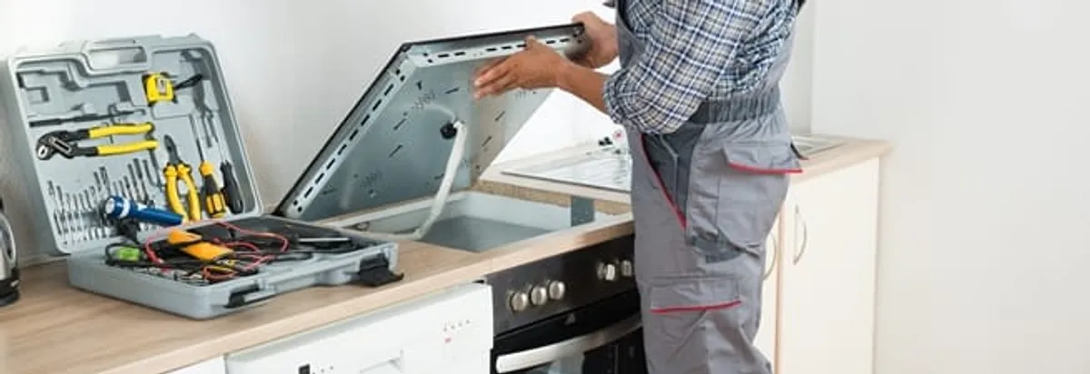 Cooktop repair technician lifting a built-in stovetop for service in Clearwater, FL